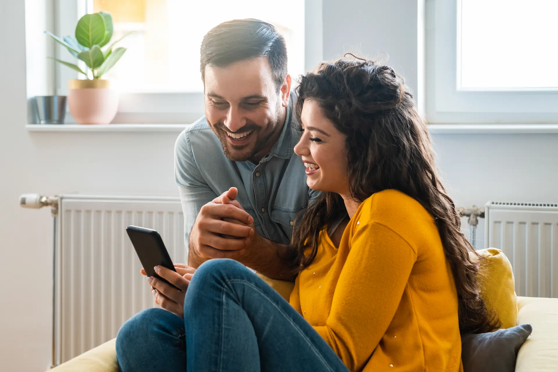 A smiling couple on a couch, the woman showing the man a fast quote on the phone screen