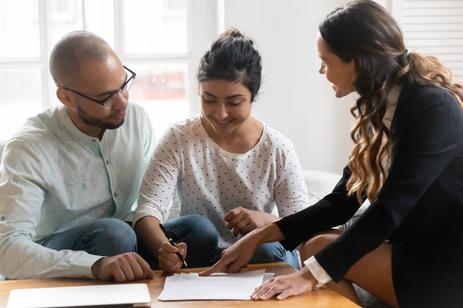 Happy couple being assisted with signing papers by their expert broker pointing where to sign